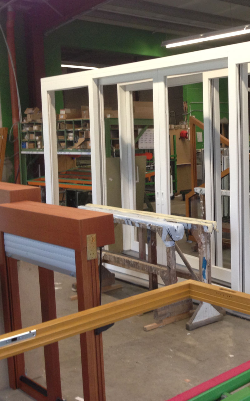 Weiße Fensterrahmen auf einem Arbeitstisch in einer Werkstatt, umgeben von verschiedenen Werkzeugen und Baumaterialien, im Prozess der Montage oder Reparatur.
